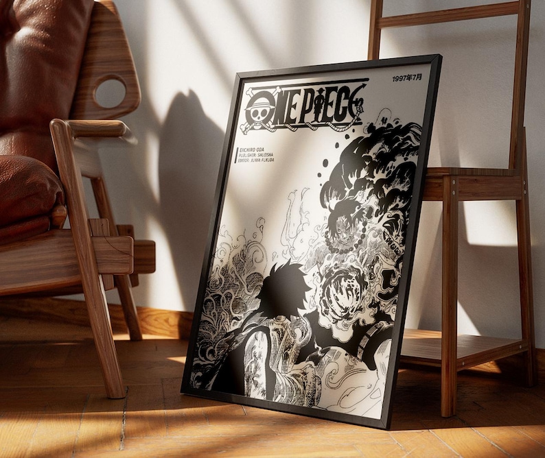 May include: Black framed poster featuring the "ONE PIECE" logo and manga artwork. The poster has a black and white illustration of a character with detailed shading and Japanese text. The poster is leaning against a wall near a wooden chair and shelf.
