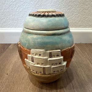 Jarra de cerámica Hopi-Tewa de alto relieve, con tapa que representa un paisaje del suroeste y la figura de un kachina con rostro de sol.