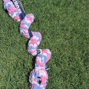 May include: A plush snake toy made of variegated pink, blue, and white yarn wrapped around a dark blue Worth baseball bat. The snake features a head with dark eyes and a pink forked tongue, with its body coiled around the length of the bat.