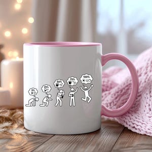 K&ouml;nnte beinhalten: Wei&szlig;e Keramiktasse mit rosa Innenraum und Henkel. Die Tasse zeigt eine schwarz-wei&szlig;e Grafik, die den Energielevel einer Person von 5 % auf 100 % mit Kaffee und Ideen steigert. Die Tasse steht auf einer Holzoberfl&auml;che.