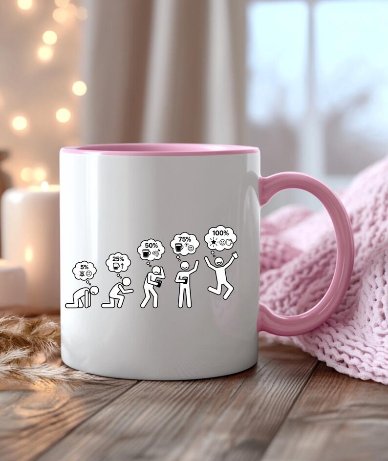 K&ouml;nnte beinhalten: Wei&szlig;e Keramiktasse mit rosa Innenraum und Henkel. Die Tasse zeigt eine schwarz-wei&szlig;e Grafik, die den Energielevel einer Person von 5 % auf 100 % mit Kaffee und Ideen steigert. Die Tasse steht auf einer Holzoberfl&auml;che.