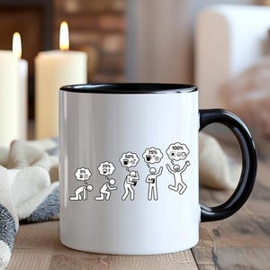 K&ouml;nnte beinhalten: Wei&szlig;e Keramik-Kaffeetasse mit schwarzem Innenraum und Griff. Die Tasse zeigt eine schwarz-wei&szlig;e Grafik, die das Energieniveau einer Person von 5 % bis 100 % darstellt, mit Kaffee und einer Gl&uuml;hbirne in Gedankenblasen. Die Tasse steht auf einer Holzoberfl&auml;che.