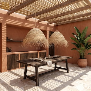 Puede incluir: Un comedor al aire libre con una mesa de madera rústica preparada para una comida. Dos lámparas colgantes tejidas cuelgan sobre la mesa. El espacio cuenta con paredes de terracota, una pérgola de madera y una gran planta en maceta.