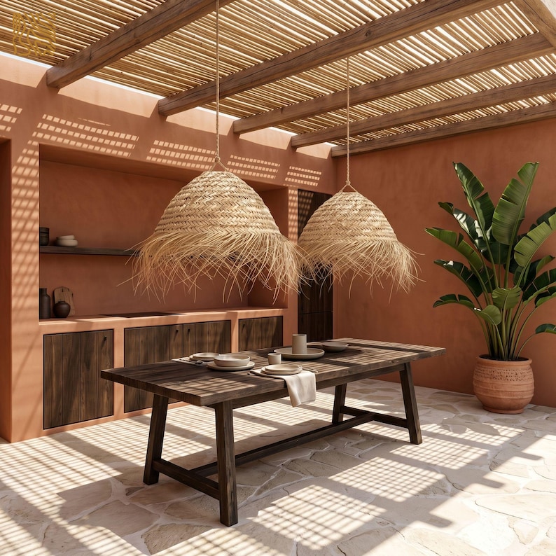 May include: An outdoor dining area with a rustic wooden table set for a meal. Two woven pendant lights hang above the table. The space features terracotta walls, a wooden pergola, and a large potted plant.