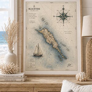 May include: A framed nautical map print with a compass rose, sailboat, and the text "BLACKTIDE". The map features a detailed illustration of an island with contour lines, in shades of blue, beige, and brown. The print is displayed on a wooden cabinet.