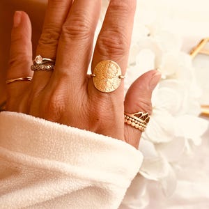 May include: A gold ring with a floral design. The ring is on a person's finger.