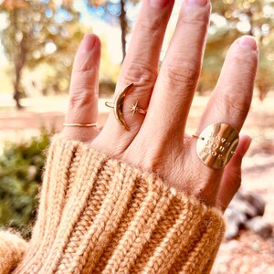 Op de afbeelding: Een hand met drie gouden ringen. De ring op de wijsvinger is een halve maan met een ster. De ring op de middelvinger is een dunne band. De ring op de ringvinger is een ronde schijf met de woorden "love you more" erop gegraveerd.