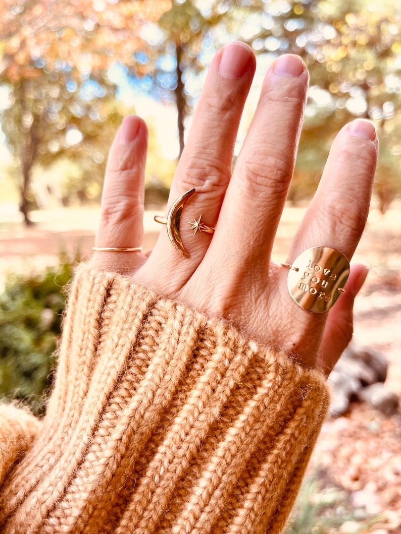 Op de afbeelding: Een hand met drie gouden ringen. De ring op de wijsvinger is een halve maan met een ster. De ring op de middelvinger is een dunne band. De ring op de ringvinger is een ronde schijf met de woorden "love you more" erop gegraveerd.