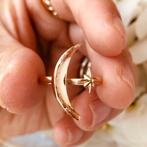 Op de afbeelding: Een gouden ring met een halve maan ontwerp en een ster accent. De ring wordt gedragen aan een vinger.