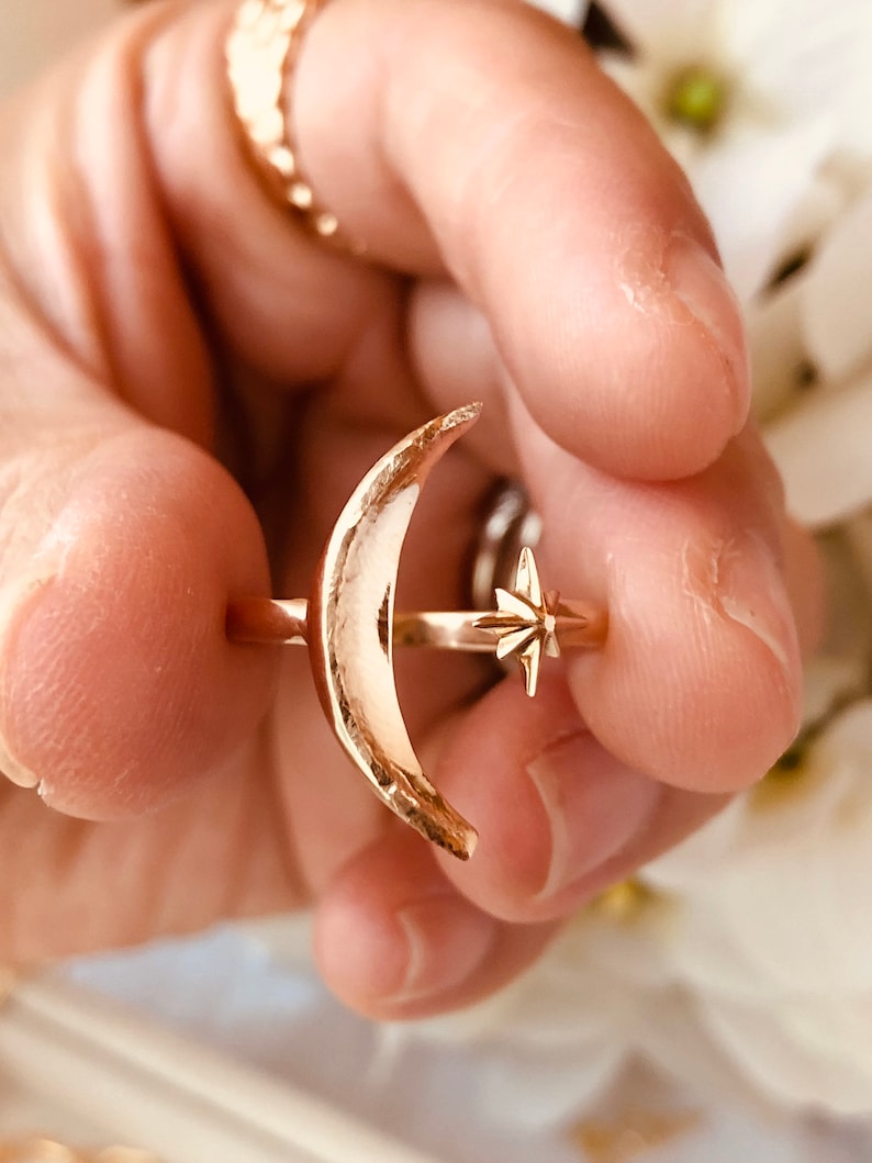 Op de afbeelding: Een gouden ring met een halve maan ontwerp en een ster accent. De ring wordt gedragen aan een vinger.