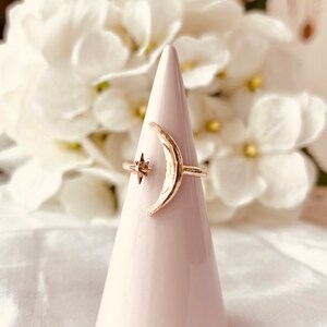 Op de afbeelding: Een gouden halve maan ring met een klein sterretje detail. De ring wordt getoond op een witte, kegelvormige ringhouder.
