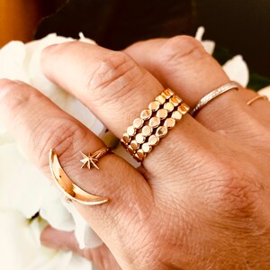 Op de afbeelding: Een gouden ring met een halve maan en ster ontwerp, gedragen op een vinger met een stapel van drie gouden ringen met een kralenontwerp.