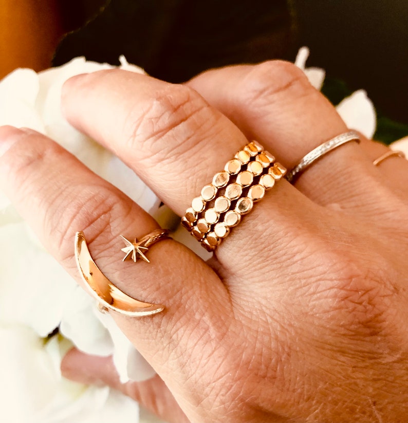 Op de afbeelding: Een gouden ring met een halve maan en ster ontwerp, gedragen op een vinger met een stapel van drie gouden ringen met een kralenontwerp.