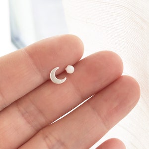 May include: A pair of silver earrings, one shaped like a crescent moon and the other a small white pearl.