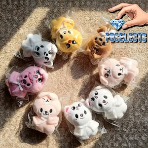 May include: A collection of plush animal toys in various colors, including yellow, pink, white, and brown. Each toy is individually packaged in clear plastic. The toys have embroidered facial features and are designed to resemble different animals.