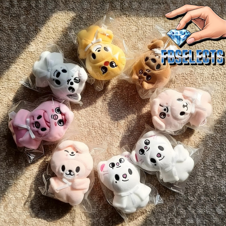 May include: A collection of plush animal toys in various colors, including yellow, pink, white, and brown. Each toy is individually packaged in clear plastic. The toys have embroidered facial features and are designed to resemble different animals.
