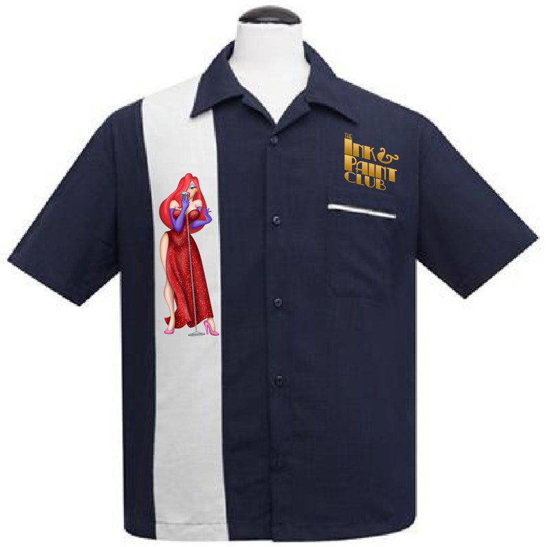 Puede incluir: Una camisa de bolos azul marino con una franja blanca en la parte delantera. El lado izquierdo de la camisa presenta una imagen de dibujos animados de una mujer con un vestido rojo. El lado derecho de la camisa tiene un logotipo dorado que dice "The Ink & Paint Club".