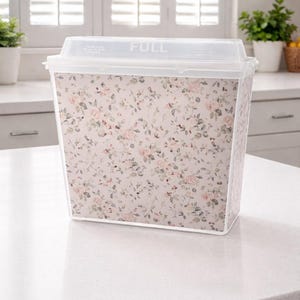 Könnte beinhalten: Ein durchsichtiger Kunststoff-Aufbewahrungsbehälter mit floralem Muster. Der Behälter hat einen Deckel mit dem Aufdruck "FULL". Das Blumenmuster zeigt rosa und grüne Rosen auf hellrosa Hintergrund.