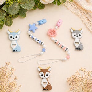 May include: Baby pacifier clips and deer-shaped teethers in blue, pink, grey, and brown. The pacifier clips have white beads with letters spelling out a name, and star or rose-shaped accents. The teethers have a heart-shaped cutout.