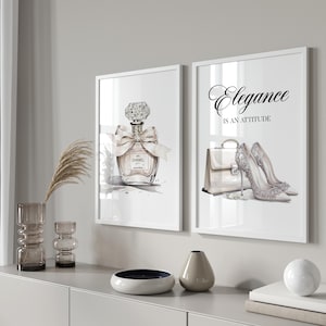 Könnte beinhalten: Zwei gerahmte Kunstdrucke. Einer zeigt einen Parfümflakon mit Schleife, der andere eine Handtasche und High Heels mit dem Text "Elegance is an attitude". Die Drucke sind in Schwarz, Weiß und Beige gehalten.