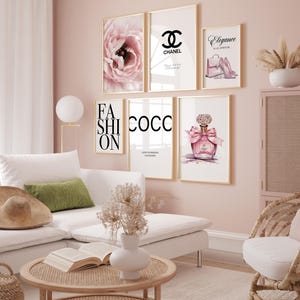 Könnte beinhalten: Eine Sammlung gerahmter Kunstdrucke mit Mode-Illustrationen und Text. Die Drucke zeigen eine rosa Blume, das Chanel-Logo, einen Parfümflakon und die Worte "Elegance is an attitude" und "Fashion". Die Farbpalette ist zartrosa und gold.