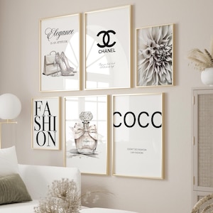 Può includere: Una collezione di stampe artistiche incorniciate con cornici dorate. Le stampe presentano illustrazioni e testo a tema moda, tra cui una borsa e tacchi, un logo Chanel, un fiore, un flacone di profumo e la parola "COCO". La combinazione di colori è nero, bianco e oro.