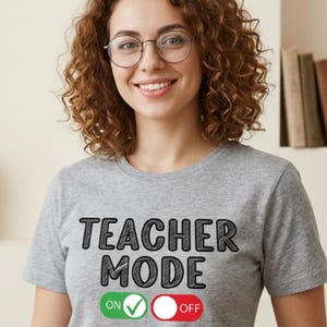 Puede incluir: Camiseta gris con la frase "TEACHER MODE" en negro. Debajo, un botón verde "ON" con una marca de verificación y un botón rojo "OFF". La persona de la imagen lleva gafas y sonríe.
