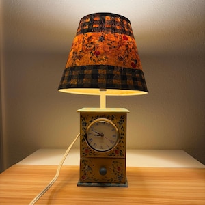 May include: A white ceramic mug with a black handle and the text "But First, Coffee" in a bold, black font. The mug is set against a blurred background, suggesting a cozy setting. The mug appears to be approximately 4 inches tall.