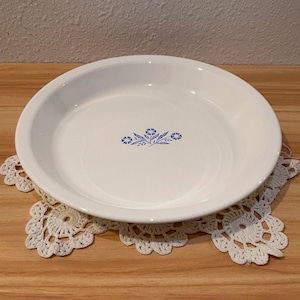 May include: A white ceramic mug with a black handle and the text "But First, Coffee" in a black, bold font. The mug is sitting on a white surface. The mug is approximately 4 inches tall.