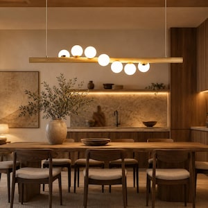 Könnte beinhalten: Ein modernes Esszimmer mit einem Holztisch und Stühlen. Über dem Tisch hängt eine Leuchte mit kugelförmigen Glühbirnen. Eine große Vase mit Grün steht auf dem Tisch. Der Raum hat eine warme, einladende Atmosphäre.