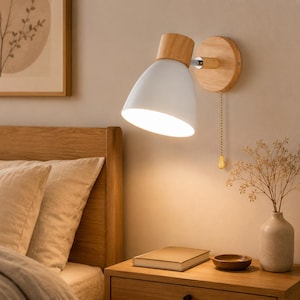Può includere: Una lampada da parete bianca e legno con una catena. La lampada ha un paralume bianco a forma di cono e una base in legno. La lampada è montata su una placca da parete in legno. La lampada è accesa, illuminando l'area.