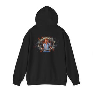 May include: Black hoodie featuring a colorful graphic of a man holding guns, set against a cosmic background. The image is centered on the back of the hoodie. The hoodie has a hood and long sleeves.