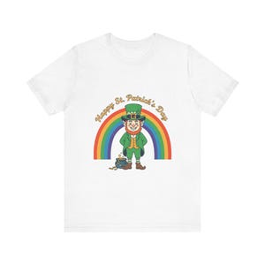 May include: White t-shirt featuring a cartoon leprechaun with a pot of gold at the end of a rainbow. The text "Happy St. Patrick's Day" is arched above the rainbow. The leprechaun is wearing a green suit and hat.