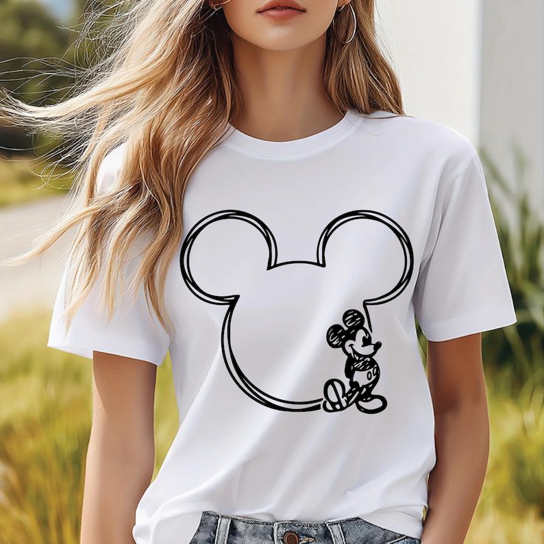 Puede incluir: Camiseta blanca con un contorno negro de la cabeza de Mickey Mouse y una ilustraci&oacute;n detallada de Mickey Mouse. El dise&ntilde;o est&aacute; centrado en la parte delantera de la camiseta.