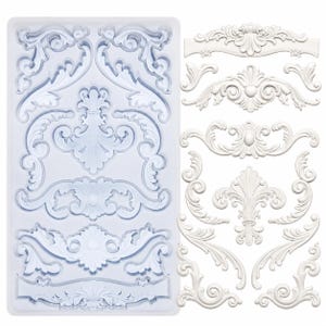 May include: A clear silicone mold with various ornate, white, baroque-style decorative elements. The mold contains several different designs, including scrolls, flourishes, and floral motifs. Separate, finished white resin pieces are displayed next to the mold.