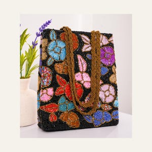 May include: A black rectangular handbag featuring an all-over beaded floral pattern in shades of blue, red, pink, and gold. The bag includes two braided gold-toned beaded handles and is constructed with a dense surface of small glass beads.