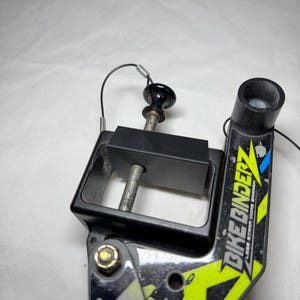 以下が含まれることがあります： 黒とネオングリーンのBike Binderz自転車アクセサリー。アクセサリーは黒いハンドル、黒い長方形のフレーム、黒いチューブを備えています。「Bike Binderz」の文字が側面に印刷されています。