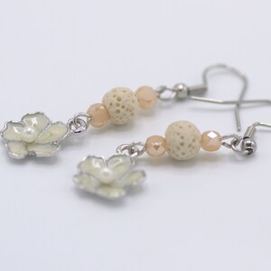May include: A pair of earrings with a flower charm and lava rock beads. The beads are a light beige color and the flower charms are white with a pearl center.