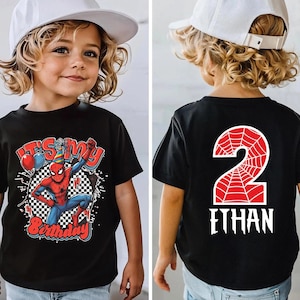 May include: Black t-shirt featuring a Spider-Man graphic with the text "It's My Birthday" and a checkered background. The back of the shirt displays a red number 2 with a spiderweb design and the name "Ethan" in white. The child is wearing a white baseball cap.