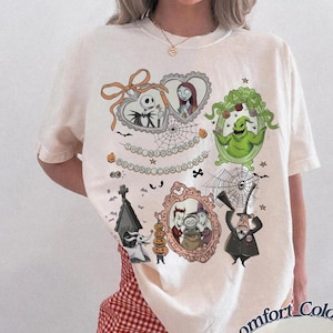 Può includere: T-shirt color avorio con diverse illustrazioni incorniciate di personaggi di "Nightmare Before Christmas". Il design include Jack Skellington, Sally, Oogie Boogie e altri personaggi, con la scritta "The Nightmare Before Christmas."
