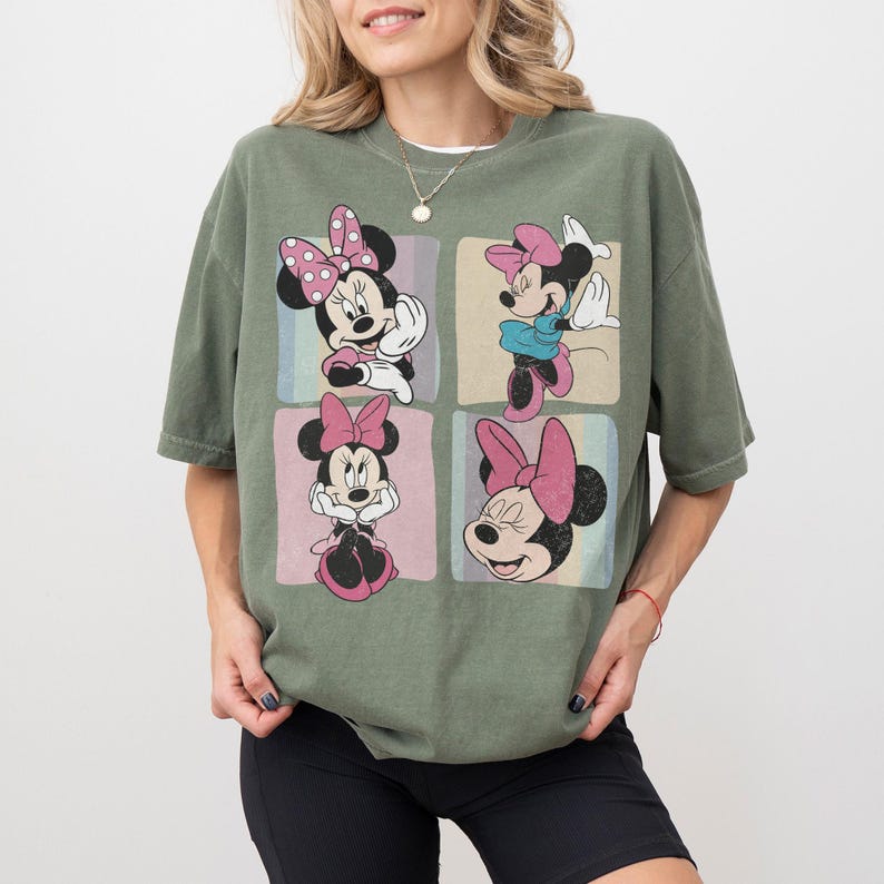 Op de afbeelding: Olijfgroen T-shirt met vier panelen met Minnie Mouse-illustraties. Elk paneel toont een andere pose van Minnie, met haar kenmerkende strik en verschillende outfits. Het T-shirt heeft een relaxte pasvorm, perfect voor casual wear.