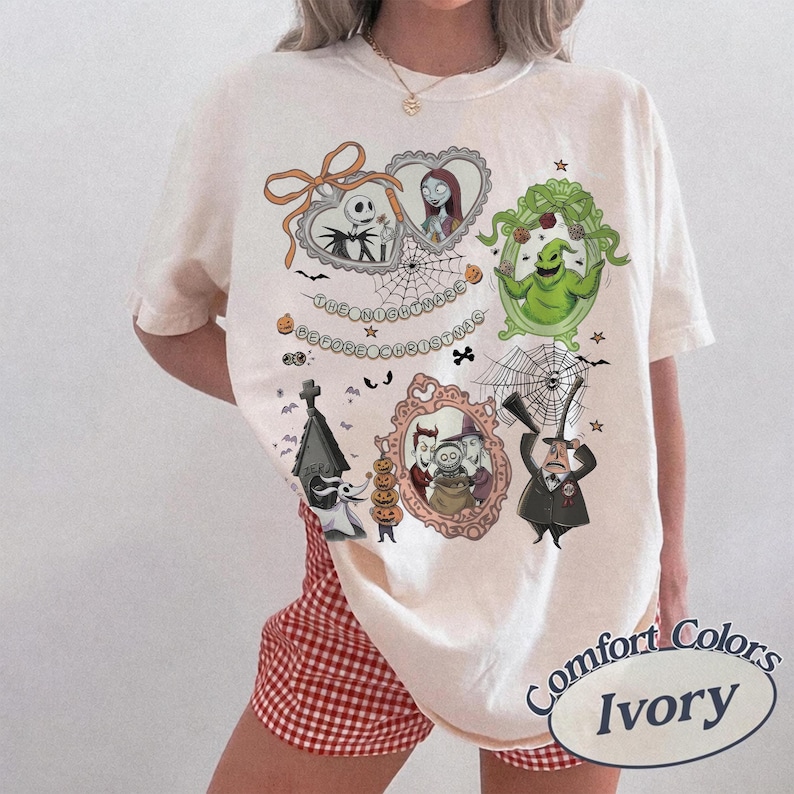 May include: Ivory-colored t-shirt featuring multiple framed illustrations of characters from "The Nightmare Before Christmas." The design includes Jack Skellington, Sally, Oogie Boogie, and other characters, with the text "The Nightmare Before Christmas."