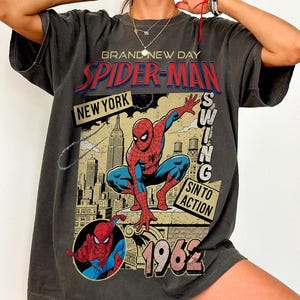 Puede incluir: Camiseta gris oscuro con un gr&aacute;fico vintage de Spider-Man. El dise&ntilde;o incluye las palabras "Spider-Man", "New York" y "1962", junto con una ilustraci&oacute;n del superh&eacute;roe. La camiseta tiene un aspecto desgastado.