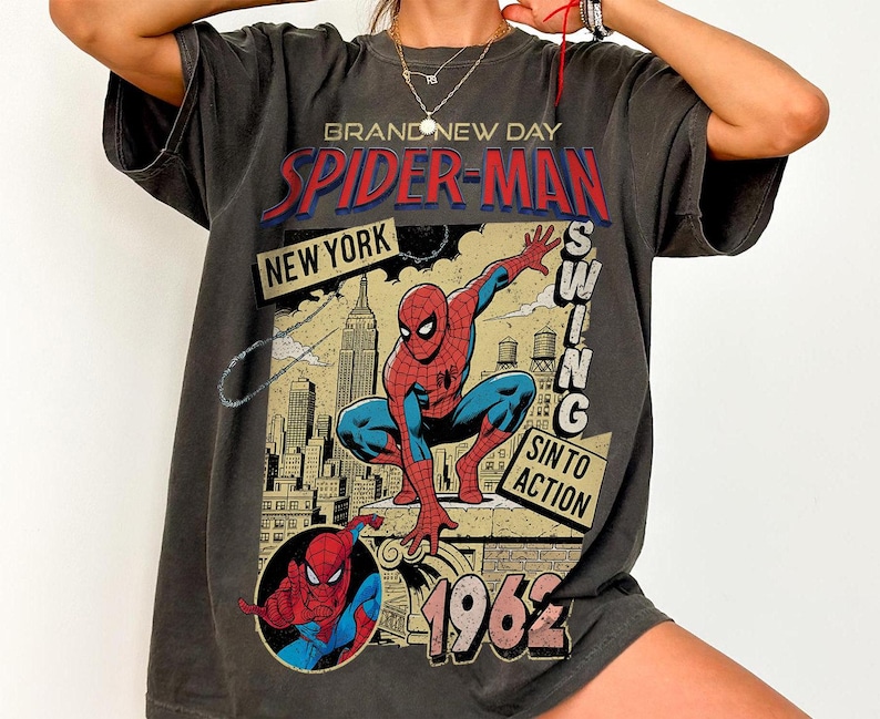 Puede incluir: Camiseta gris oscuro con un gr&aacute;fico vintage de Spider-Man. El dise&ntilde;o incluye las palabras "Spider-Man", "New York" y "1962", junto con una ilustraci&oacute;n del superh&eacute;roe. La camiseta tiene un aspecto desgastado.