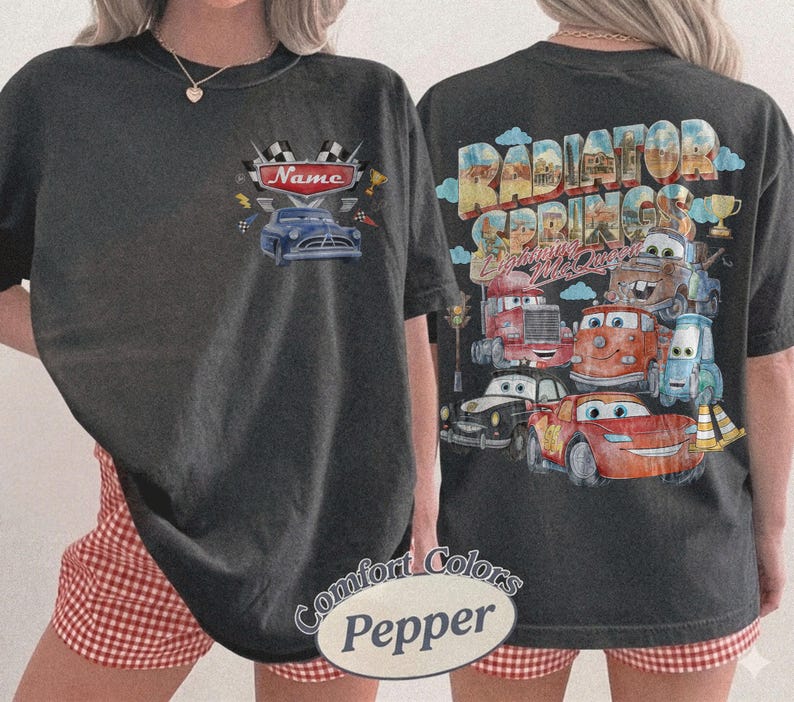 May include: A charcoal gray t-shirt featuring a small graphic on the front chest with a blue car and the text Name. The back displays a large, colorful graphic of various cartoon cars with the text Radiator Springs and Lightning McQueen.