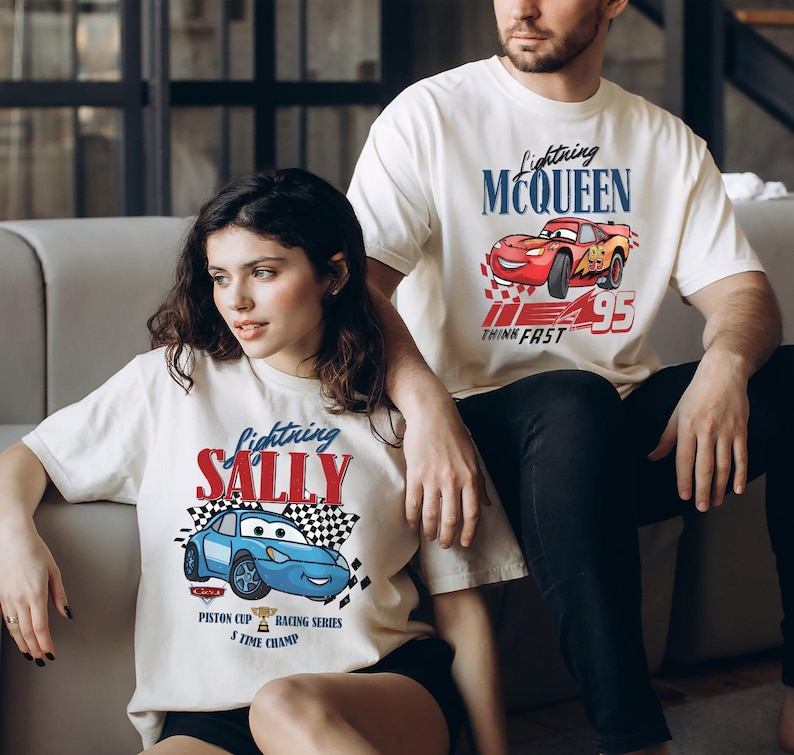 May include: Two off-white t-shirts with graphics from the film "Cars." One shows "Lightning McQueen" with a red race car, the other "Lightning Sally" with a blue race car. Both shirts include text and racing-themed designs, perfect for fans of the animated movie.