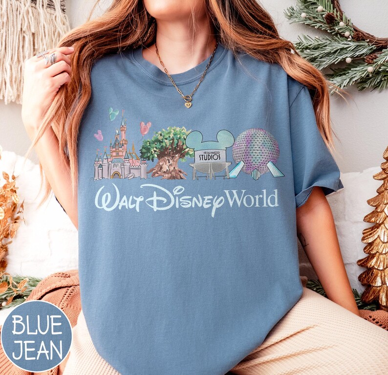 May include: Blue jean coloured t-shirt featuring a Walt Disney World graphic. The graphic includes a castle, tree, and other park icons. The words "Walt Disney World" are written in a script font.