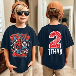 May include: Navy blue t-shirt featuring a Spider-Man graphic with the text "It's My Birthday" and a number 2 on the back. The front design includes balloons and a checkered background. A fun birthday shirt.