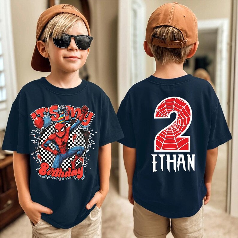 May include: Navy blue t-shirt featuring a Spider-Man graphic with the text "It's My Birthday" and a number 2 on the back. The front design includes balloons and a checkered background. A fun birthday shirt.