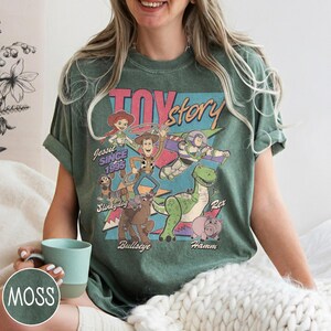 May include: Green t-shirt with a Toy Story graphic featuring Woody, Buzz Lightyear, and Rex. The text "Toy Story" and "Jessie Since 1995" are displayed. The shirt has a vintage, distressed appearance.